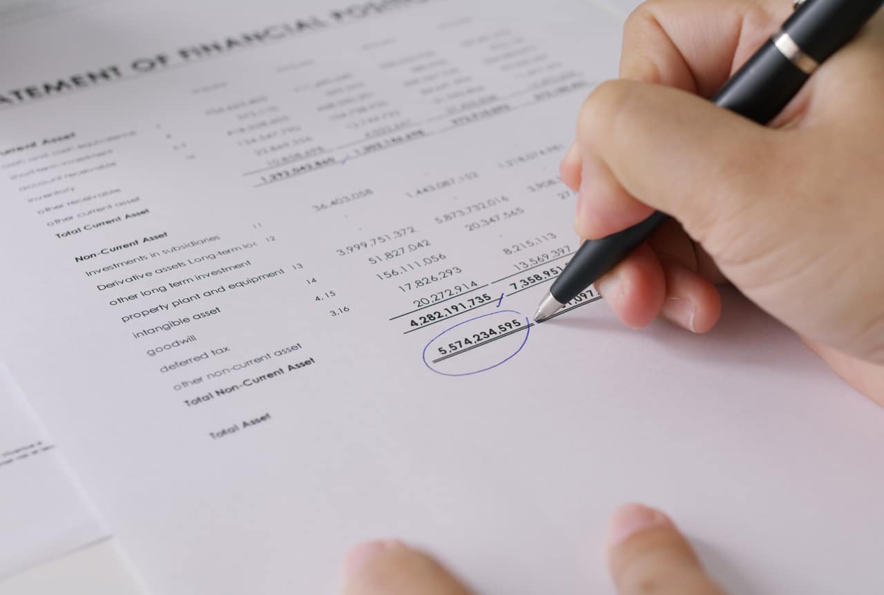 A close-up of a hand holding a black pen, analyzing a financial statement with key figures circled, representing balance sheet protection and financial planning.