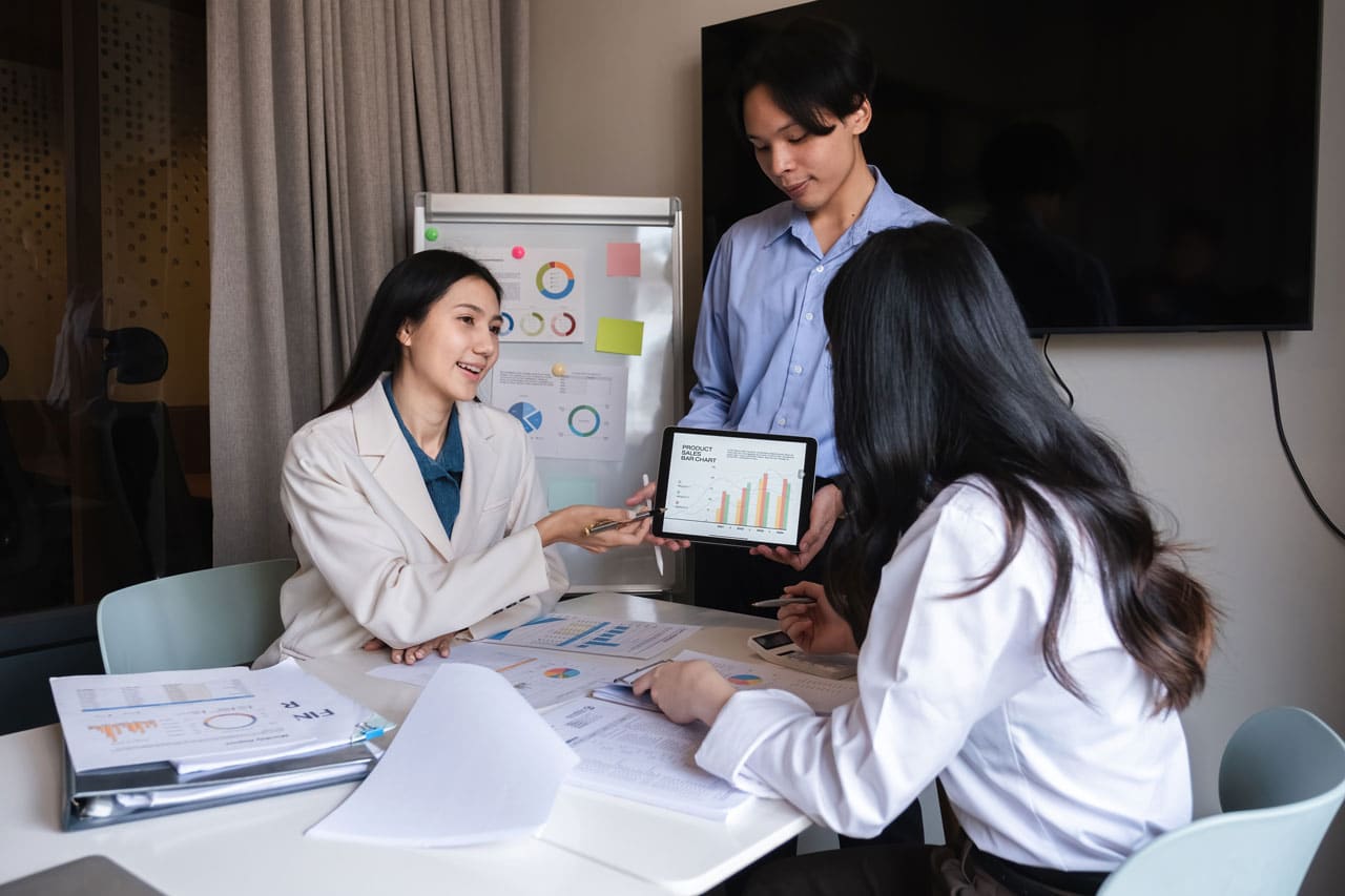 Three professionals analyzing financial charts and graphs during a Mid-Year Wealth Check-Up meeting.