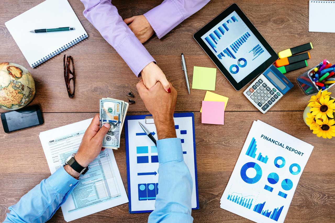 Financial Partnership illustrated by professionals shaking hands while reviewing financial reports and data together